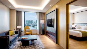 A hotel room with a bed, a sofa, a chair, a coffee table, a TV, and a large window with a city view.