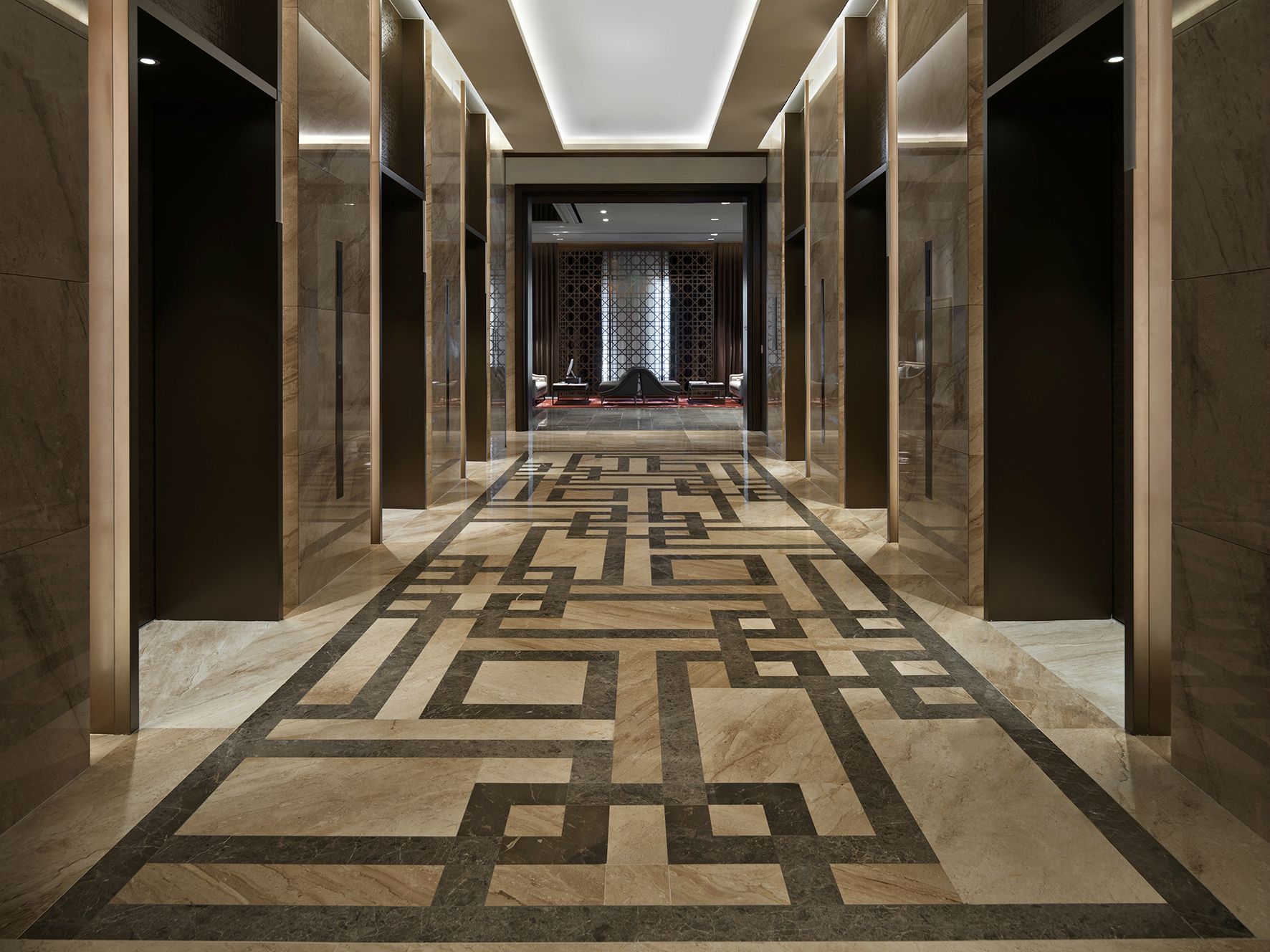 A hallway with a geometric patterned floor, marble walls, and a modern ceiling design.