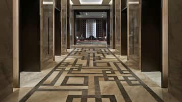 A hallway with a geometric patterned floor, marble walls, and a modern ceiling design.