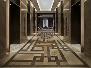 A hallway with a geometric patterned floor, marble walls, and a modern ceiling design.