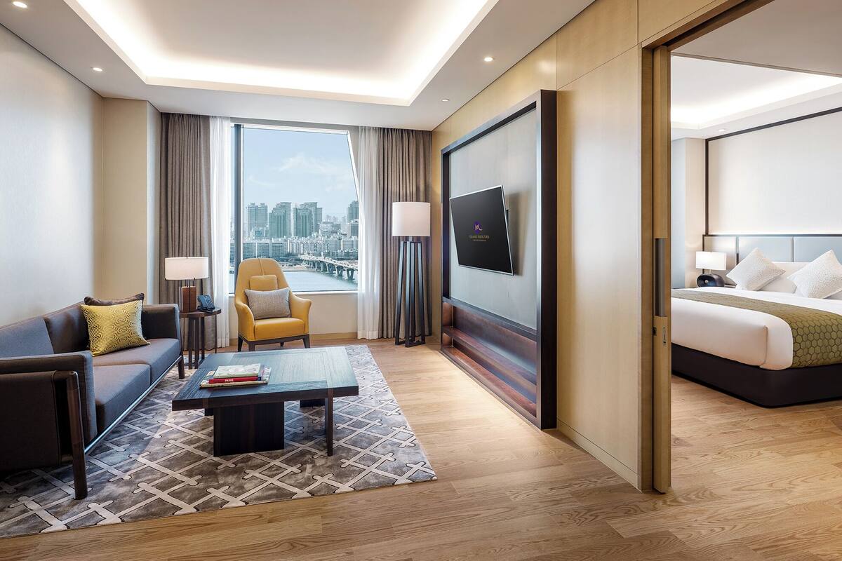 A hotel room with a sofa, armchair, coffee table, and a bed.