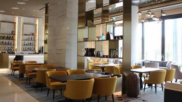 A modern dining area with yellow chairs and tables, a bar with shelves of bottles, and a large mirror reflecting the space.