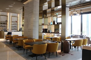 Ein moderner Essbereich mit gelben Stühlen und Tischen, eine Bar mit Flaschenregalen und ein großer Spiegel, der den Raum widerspiegelt.