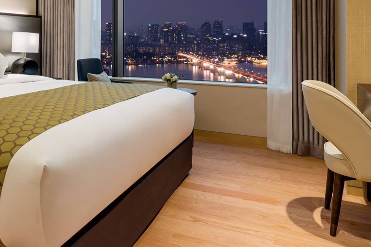 A hotel room with a large bed, a desk, a chair, and a view of a cityscape at night.