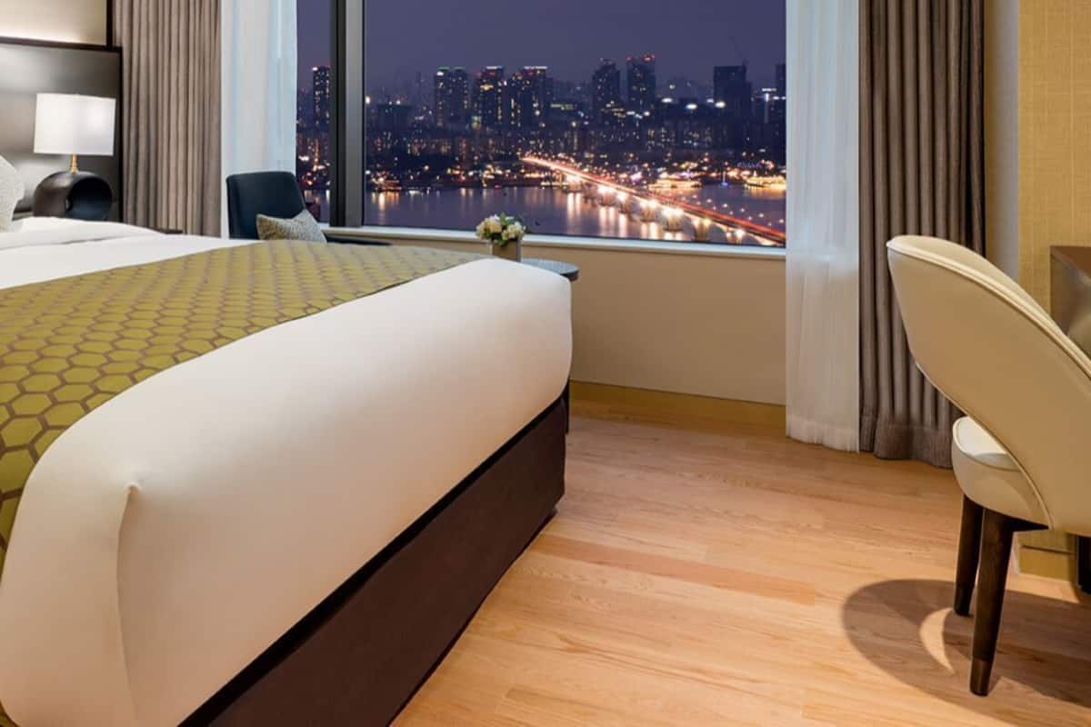 Une chambre d’hôtel avec un grand lit, un bureau, une chaise et une vue sur le paysage urbain illuminé la nuit.