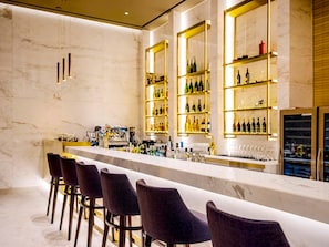 Um bar com paredes de mármore, prateleiras cheias de garrafas e banquetas.