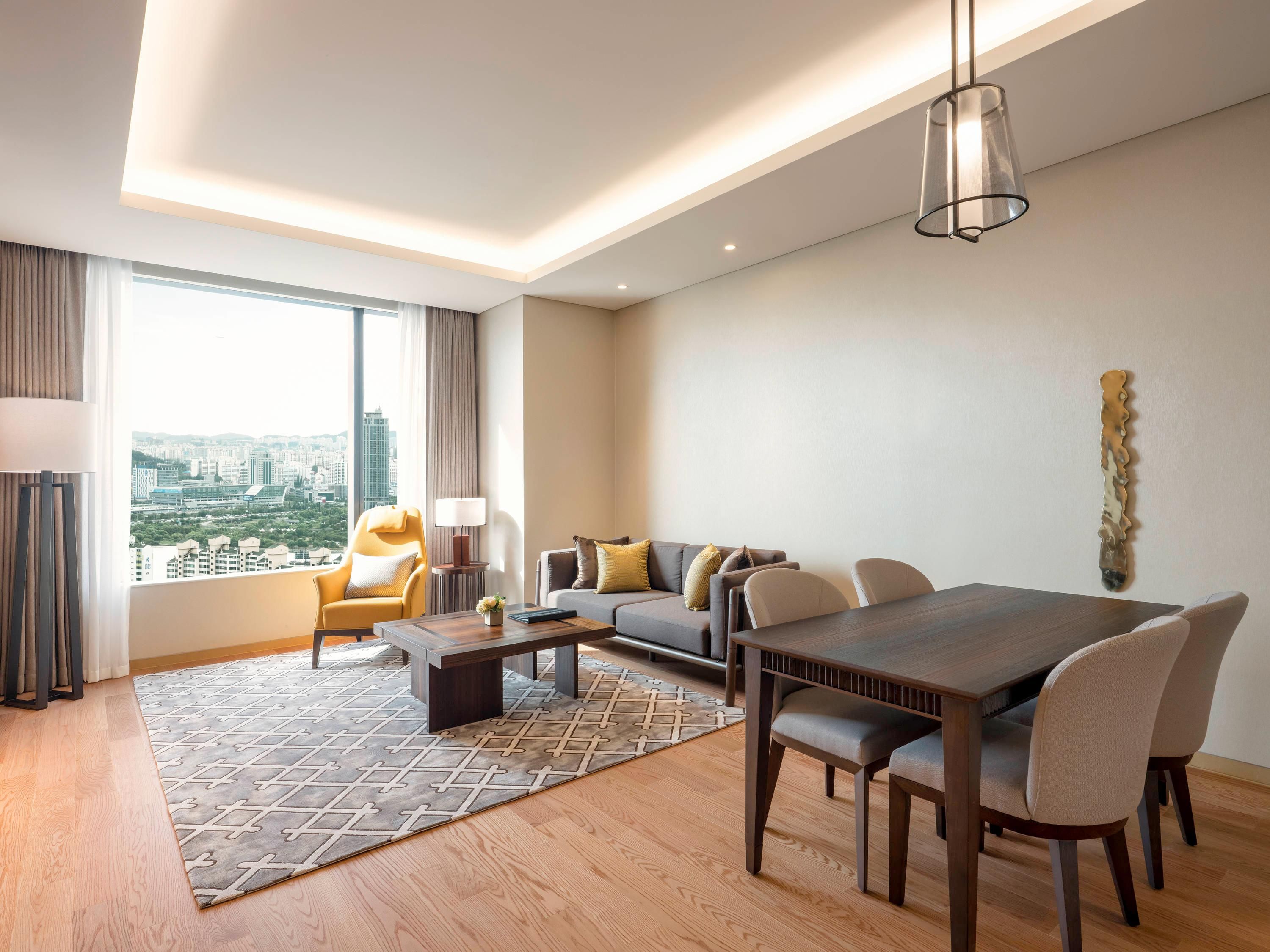 Habitación de hotel moderna con zona de comedor, un conjunto de sofás, una mesa de centro y vistas a la ciudad.