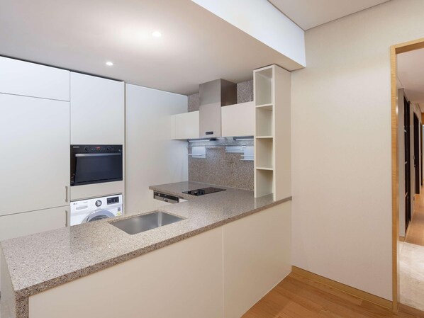 Cozinha compacta com eletrodomésticos embutidos, bancada de granito e piso de madeira.