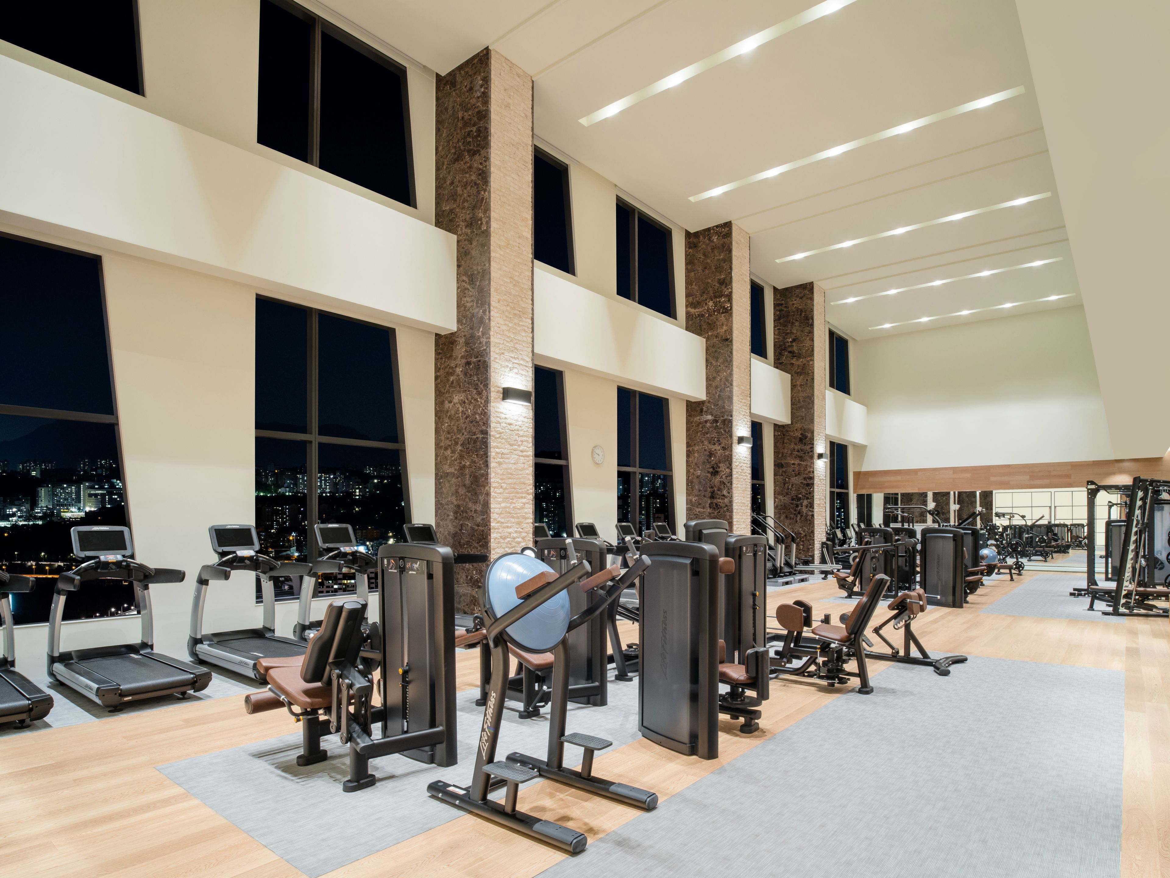 Une salle de sport équipée de tapis de course, d’appareils de musculation et offrant une vue sur la ville.