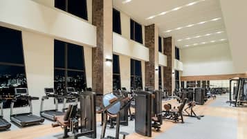 Une salle de sport équipée de tapis de course, d’appareils de musculation et offrant une vue sur la ville.