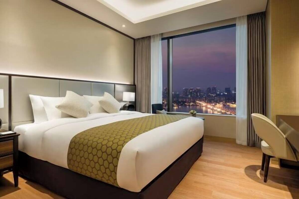 A hotel room with a large bed, a desk, a chair, and a city view.