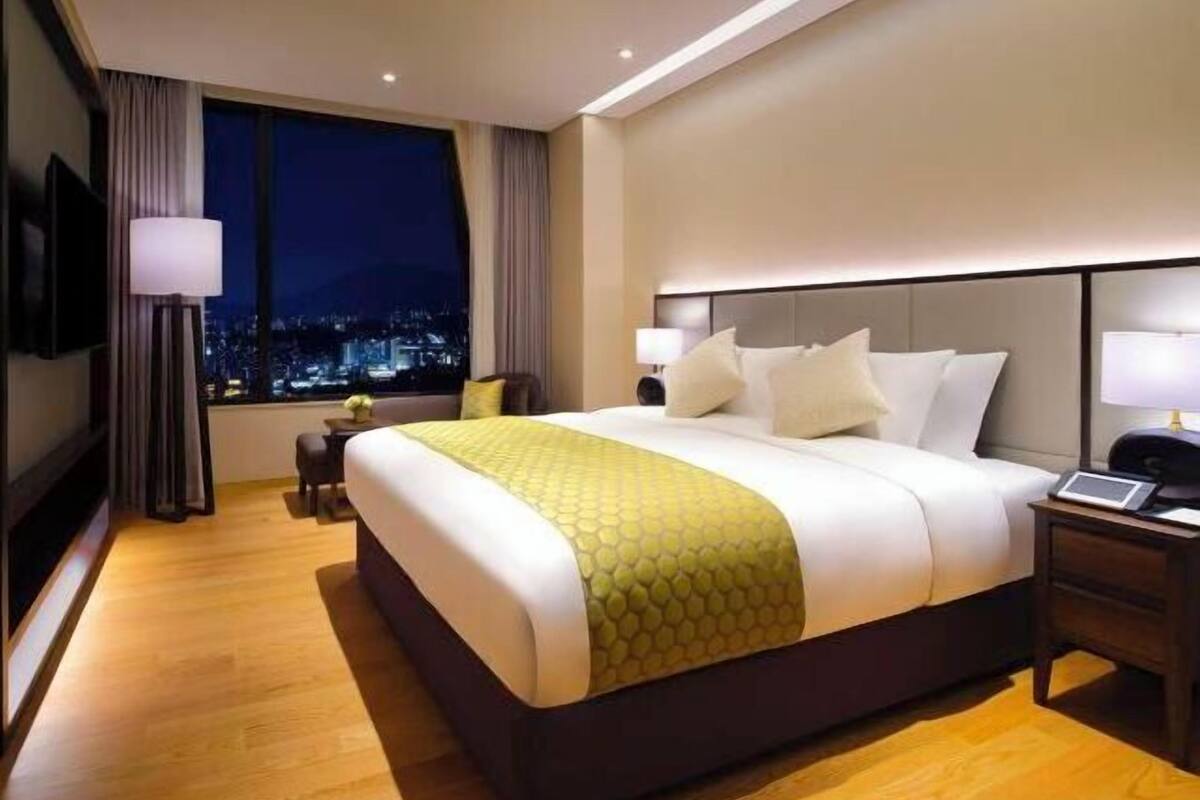 A hotel room with a large bed, bedside tables, a TV, and a view of the city at night.