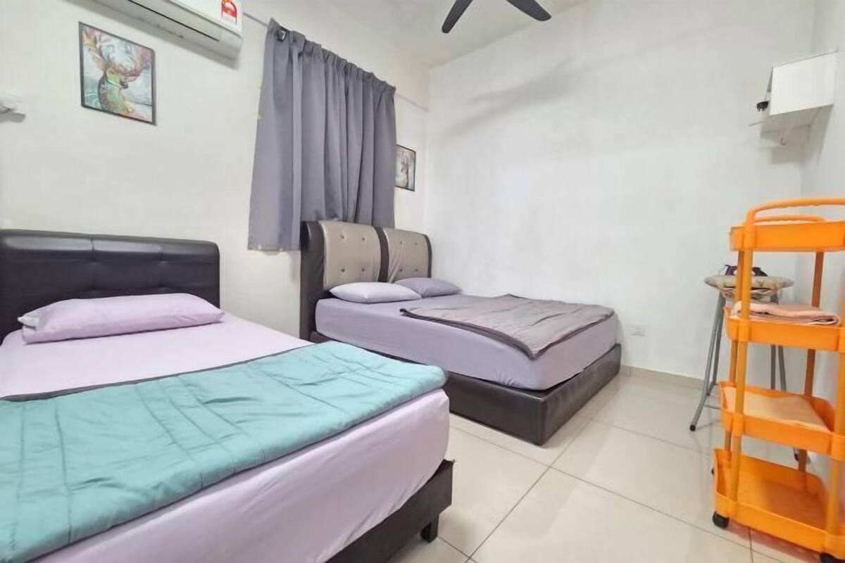 Ein Zimmer mit zwei Betten, einem Deckenventilator, einem Fenster mit Vorhängen und einem kleinen orangefarbenen Wagen.