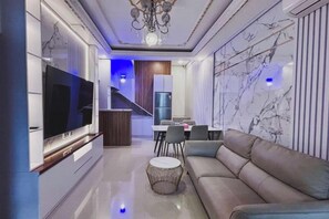Een moderne woonkamer met een flatscreen televisie, een bank, een salontafel en een eethoek met stoelen.