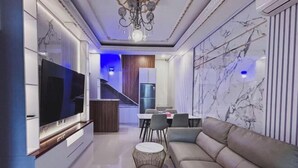 Una sala de estar moderna con un televisor de pantalla plana, un sofá, una mesa de centro y un comedor al fondo.