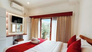 Habitación de hotel con cama, televisor montado en la pared y ventana con cortinas.