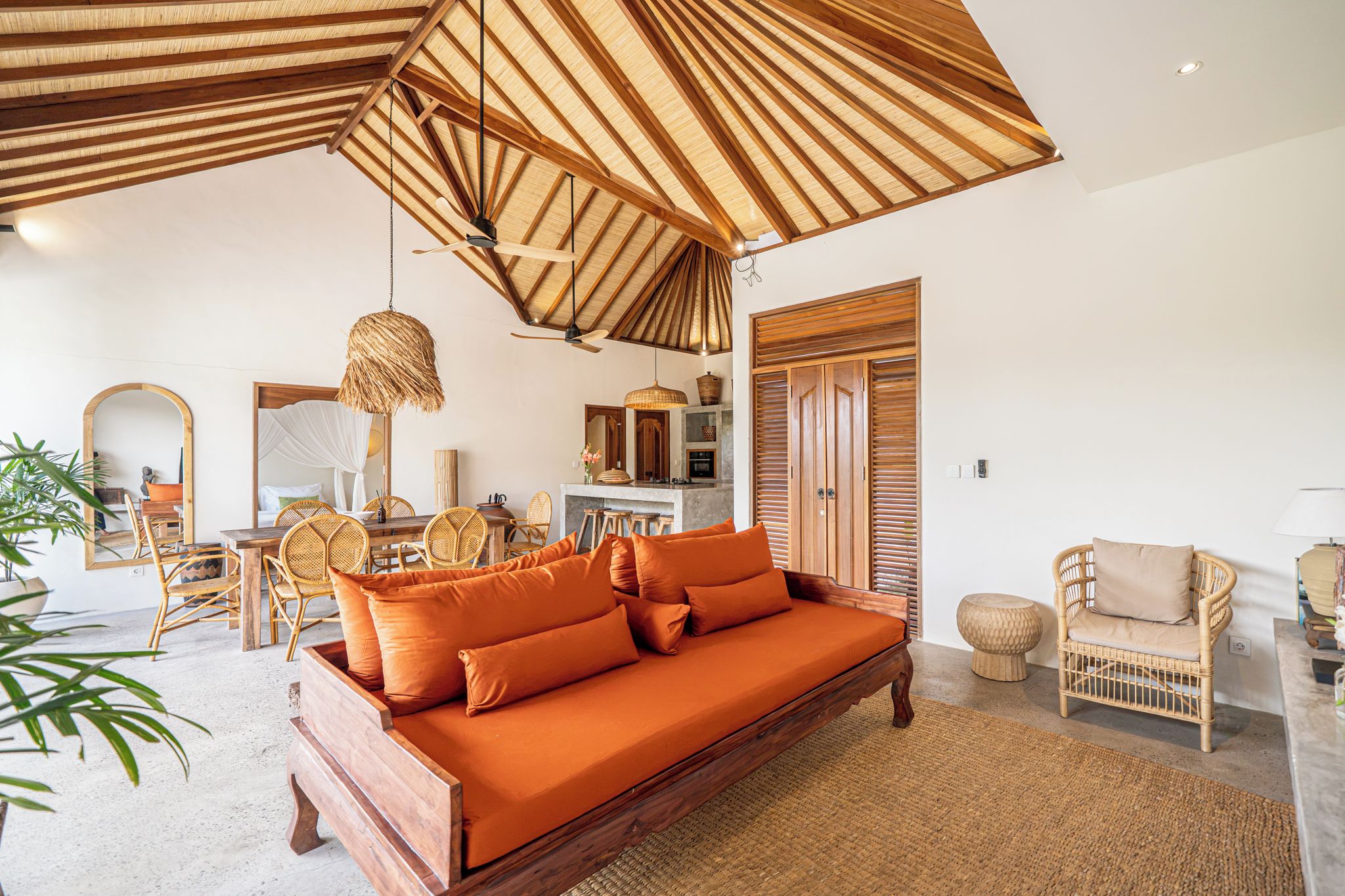 Un salón amplio con un sofá de madera, sillas de mimbre y una mesa de comedor.