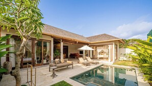 Un espace aménagé au bord de la piscine, comprenant une chaise longue, une petite table et un coin salon abrité.