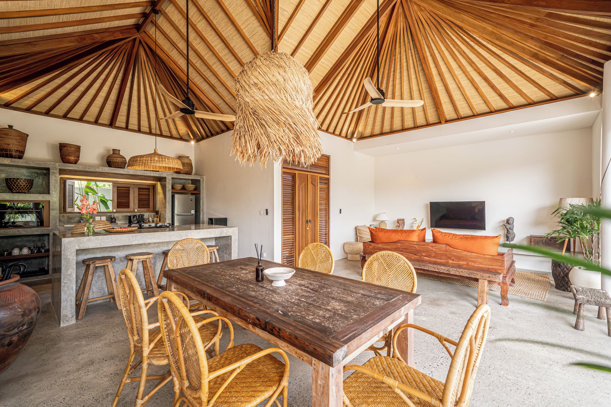 Een ruime woonkamer met een houten eettafel, rieten stoelen, een bank en een televisie.