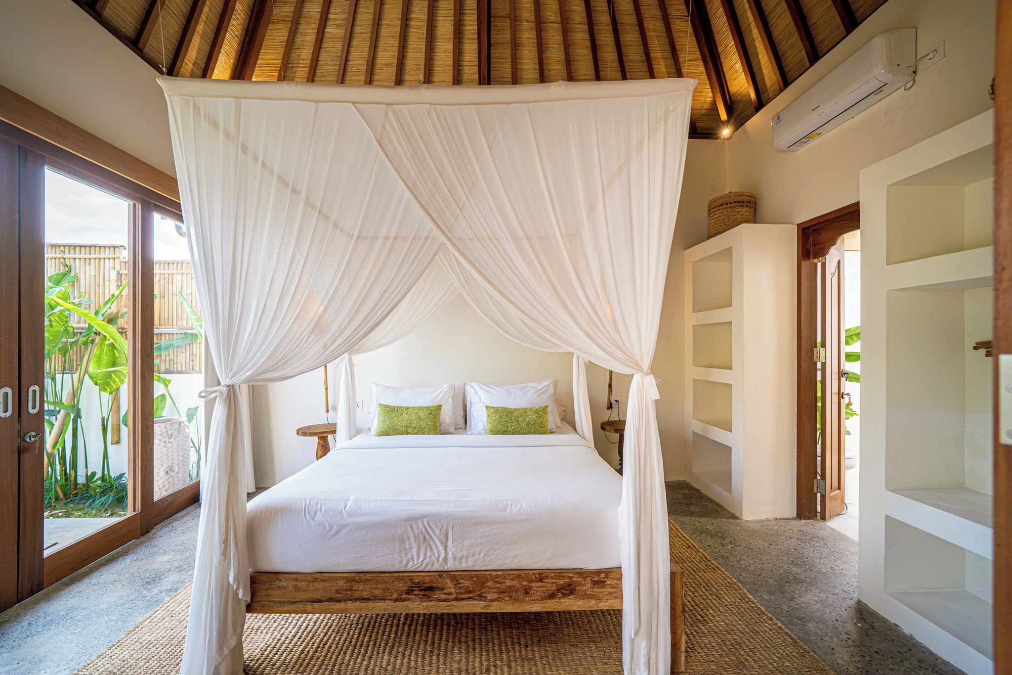 A bedroom with a four-poster canopy bed, a wooden headboard, and a large window with a view of greenery outside.