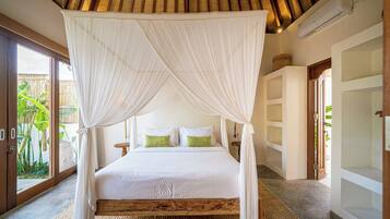 A bedroom with a four-poster canopy bed, a wooden headboard, and a large window with a view of greenery outside.