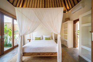 A bedroom with a four-poster canopy bed, a wooden headboard, and a large window with a view of greenery outside. - Casa Nyang Uluwatu (Pecatu)