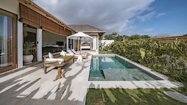Uma área de piscina moderna ao ar livre, com espreguiçadeira, mesa pequena e toldo.