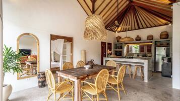 A spacious dining area with a wooden table and wicker chairs, a kitchen with modern appliances, and a large mirror reflecting the room.
