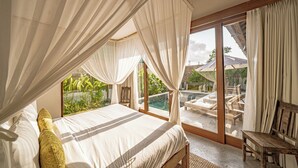 Une chambre dotée d’un grand lit, offrant une vue sur une piscine et comprenant un balcon aménagé avec du mobilier d’extérieur.
