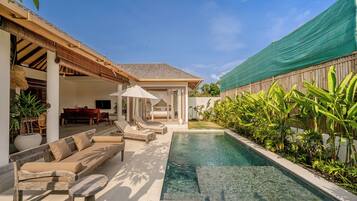 Un área junto a la piscina con sillones, una zona de estar techada y un dormitorio con vistas a la piscina.