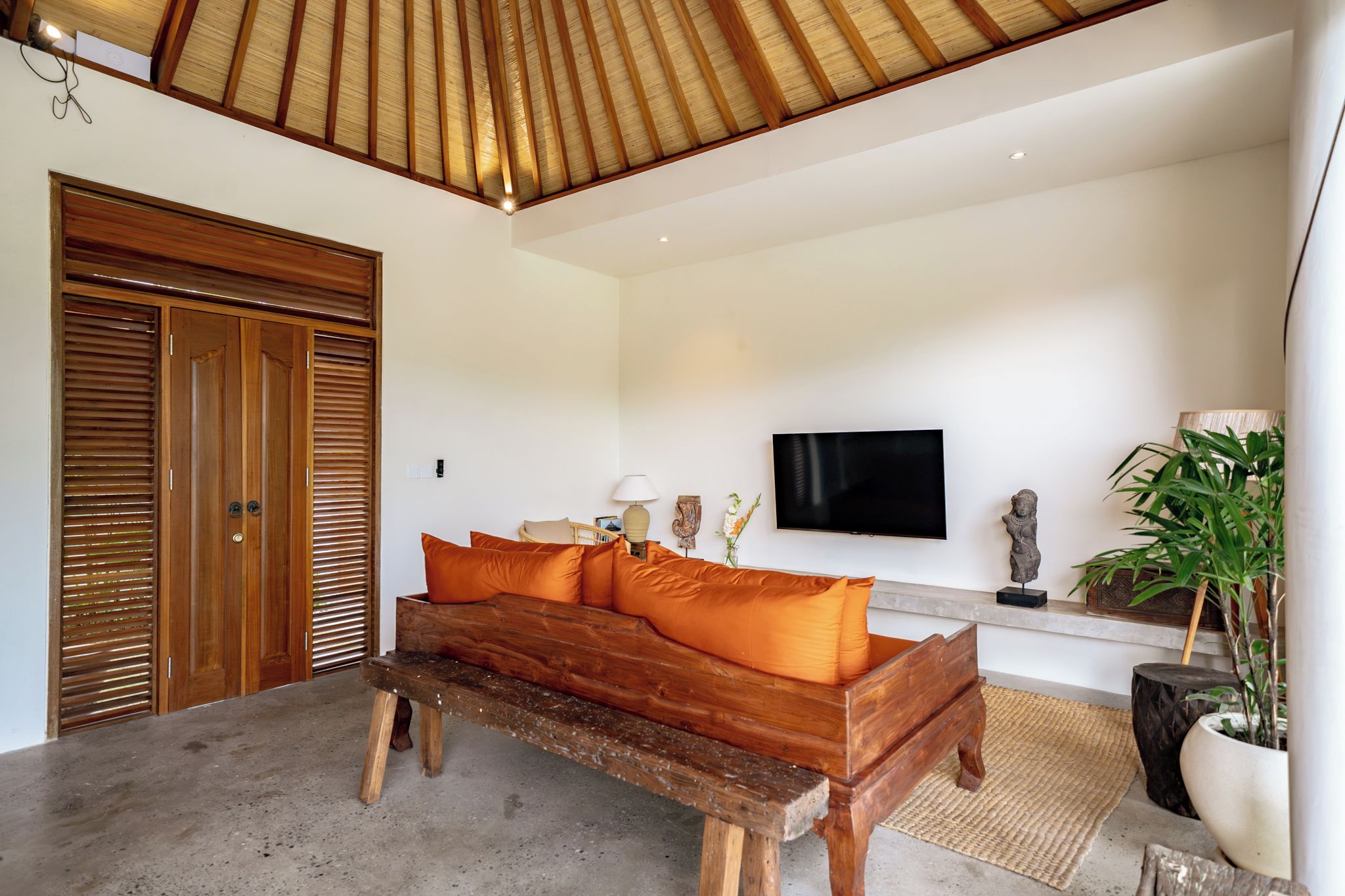 Una habitación con un banco de madera, un sofá con cojines naranjas, un televisor y una estatua en un estante.