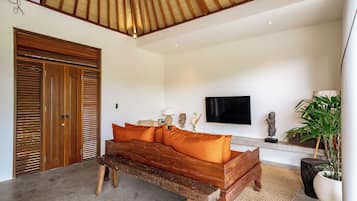 A room with a wooden bench, a sofa with orange cushions, a television, and a statue on a shelf.