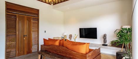 Una habitación con un banco de madera, un sofá con cojines naranjas, un televisor y una estatua en un estante.