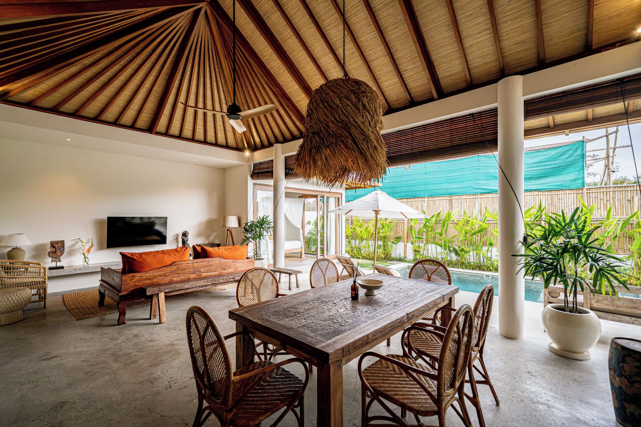 Amplia sala de estar con una gran mesa de madera, asientos cómodos, televisión y vista a una piscina.