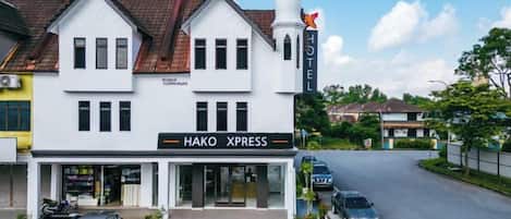 Un hotel con un cartel que dice 'Hako Xpress' y un estacionamiento con varios coches.
