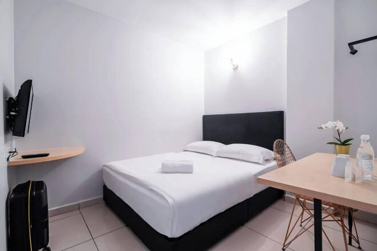 Hotellihuone, jossa on sänky, työpöytä, tuoli, televisio, hylly ja ruukkukasvi.