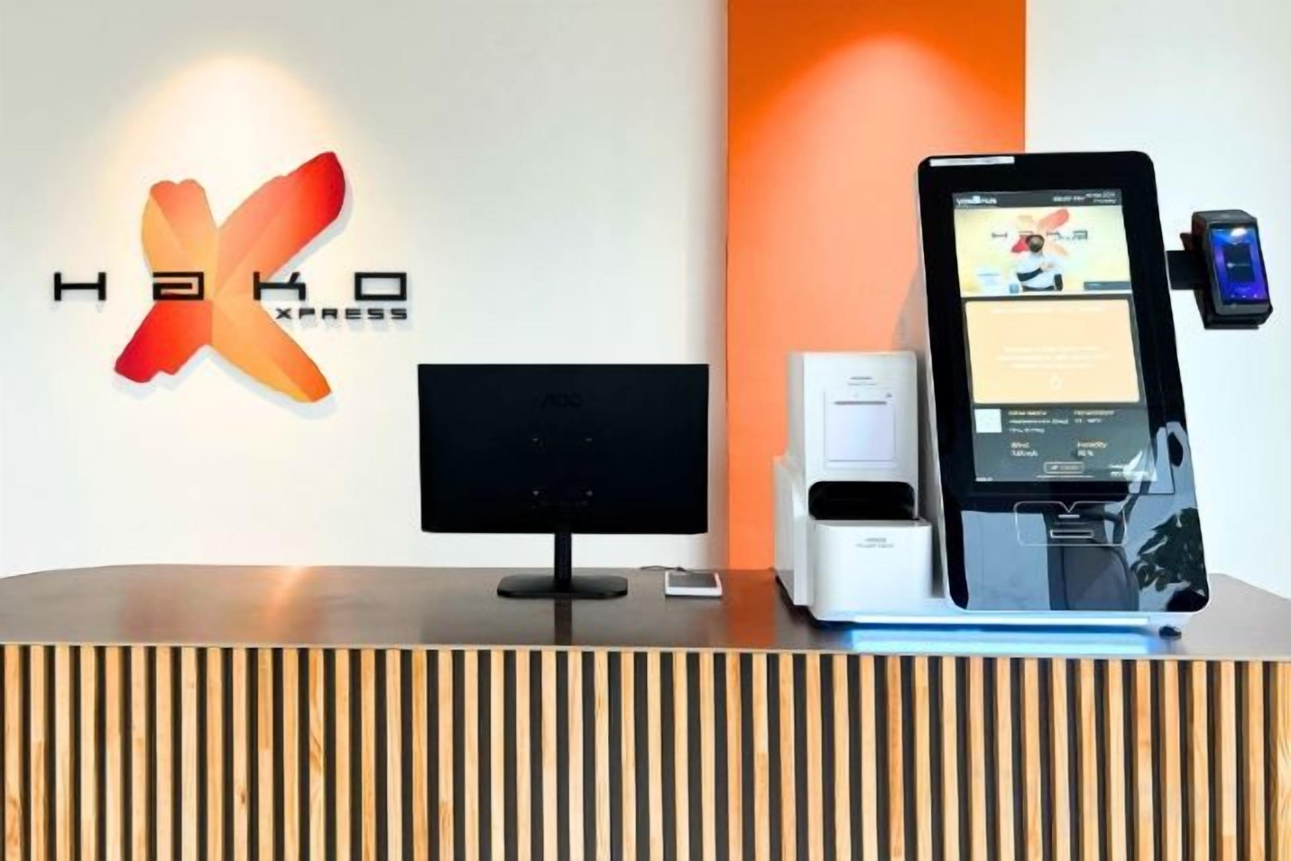 A reception desk with a digital kiosk, a flat-screen monitor, and a coffee machine.