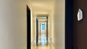 A hotel hallway with a light-colored floor, a dark door on the right, and a window at the end. - Hako Xpress Tampoi (Johor Bahru)