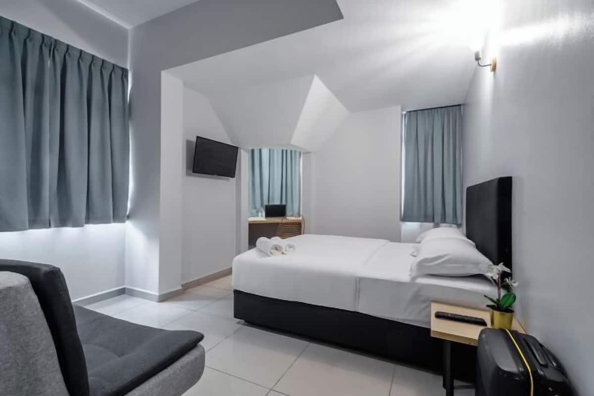 Moderni hotellihuone, jossa on sänky, työpöytä, tuoli ja seinälle asennettu televisio.