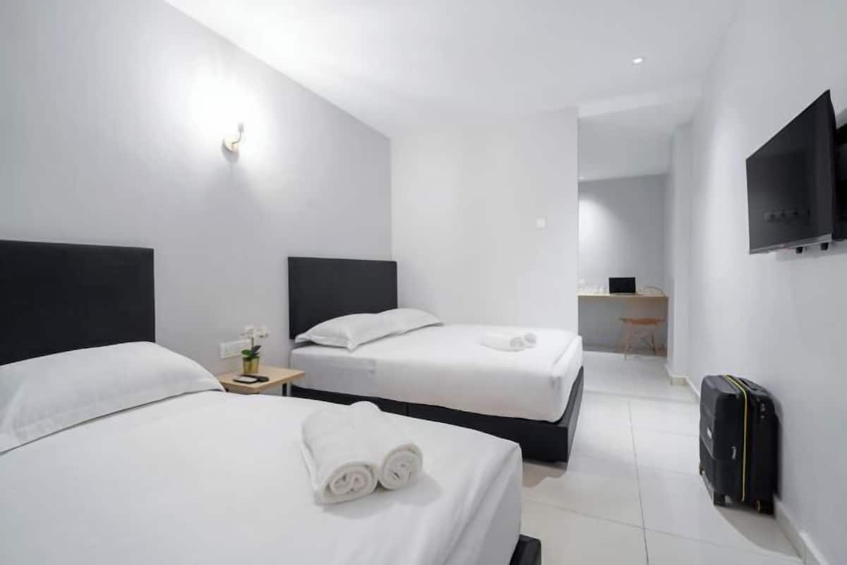 Hotellihuone, jossa on kaksi sänkyä, työpöytä, tuoli, televisio ja matkalaukku.