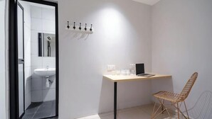 A modern bathroom with a sink, mirror, and a shower. There's a wooden desk with a chair and a laptop. - Hako Xpress Tampoi (Johor Bahru)
