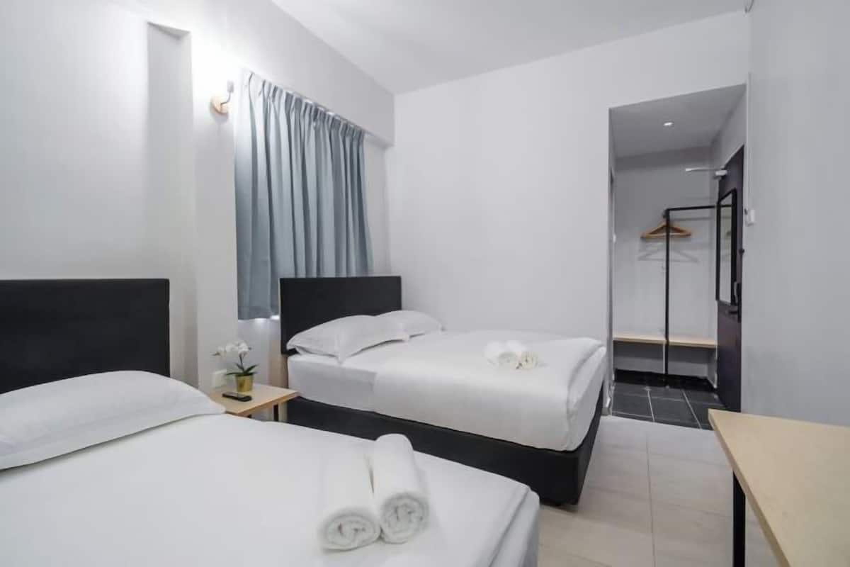 Moderni hotellihuone, jossa on kaksi sänkyä, pieni pöytä ja suihkutila.