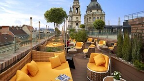 A rooftop terrace with wicker furniture, a sofa, and a view of historic buildings. - Aria Hotel Budapest by Library Hotel Collection (Budapest)