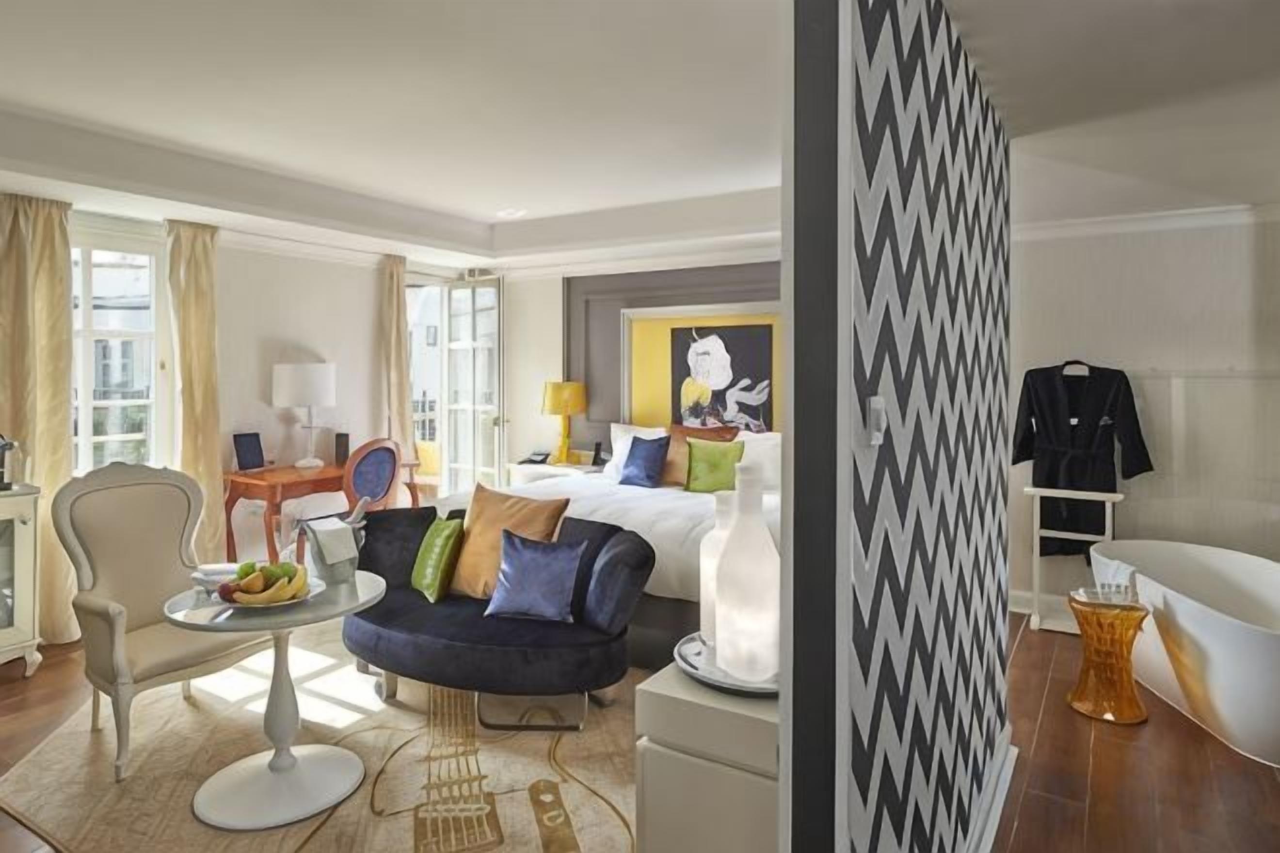 A hotel room with a bed, a sofa, a dining table, and a small kitchen area.