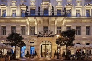 Une façade imposante d’hôtel, avec une entrée centrale, des balcons et des espaces de détente en plein air.