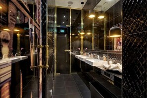 Un baño moderno con varios lavamanos, un espejo y una puerta de cristal.