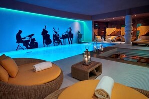 Un salon au bord de la piscine, avec un mur illuminé de lumière bleue, une piscine et des fauteuils confortables.