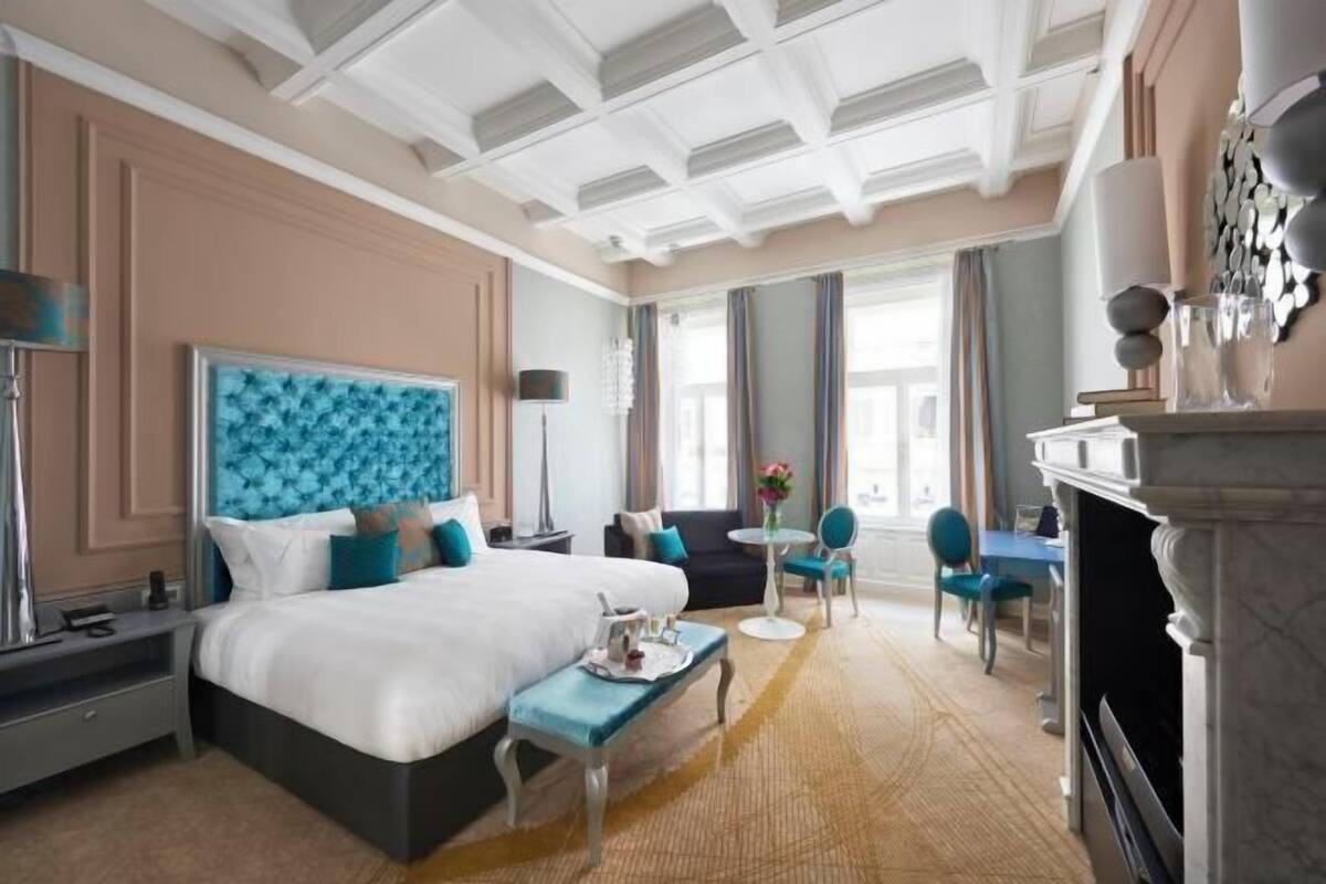 Ett hotellrum med en stor säng, ett skrivbord, en stol, ett litet bord och en öppen spis.