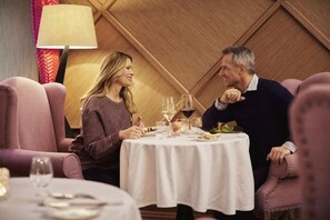 A couple dining at a round table with a white tablecloth, surrounded by plush chairs, in a room with wooden paneling. - Aria Hotel Budapest by Library Hotel Collection (Budapest)