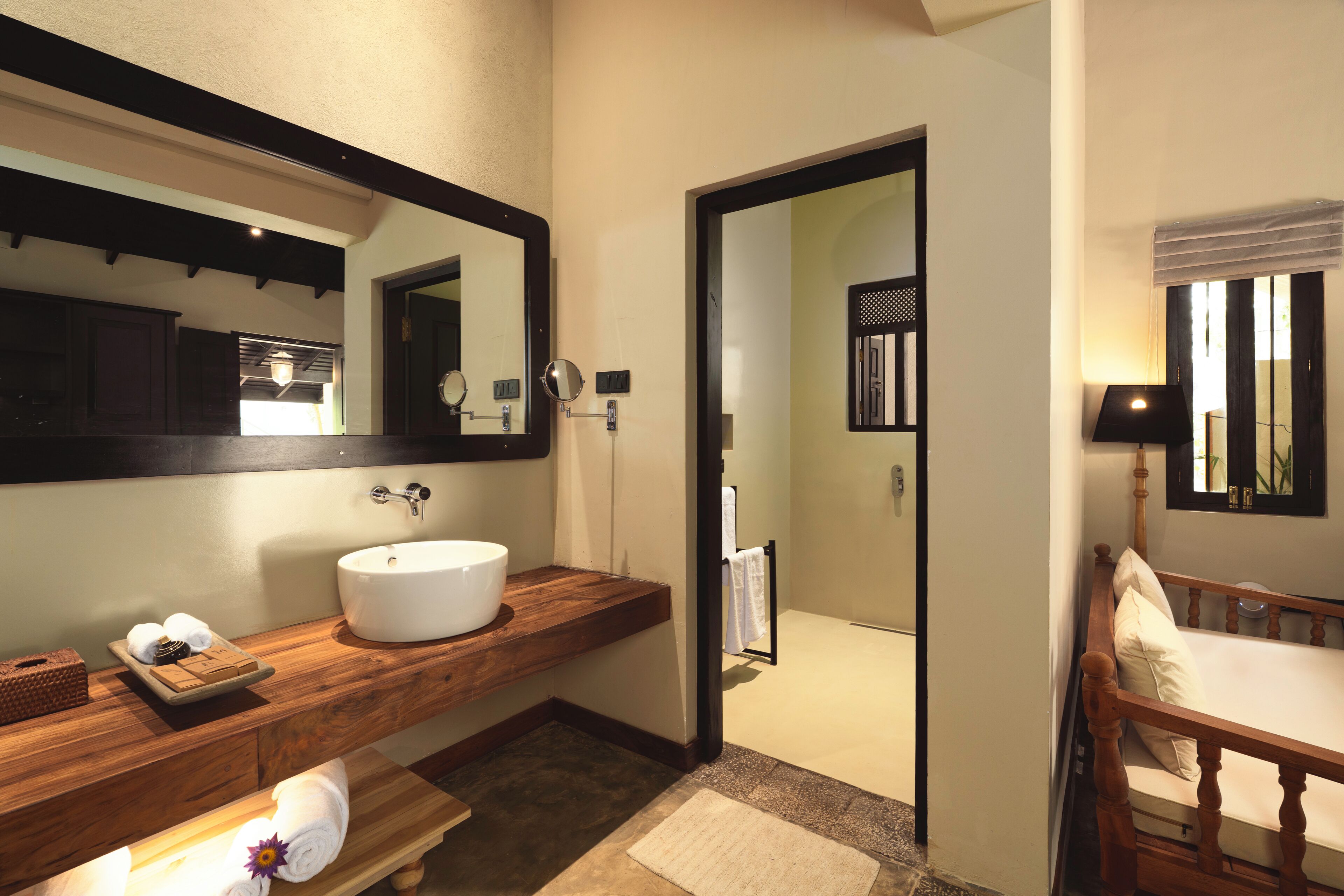 A bathroom with a wooden vanity, a white sink, a mirror, and a wooden bed.